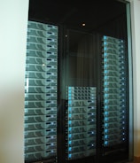 A server room or data center featuring several racks of network servers with blue indicator lights. The setup is organized and enclosed within a glass cabinet.