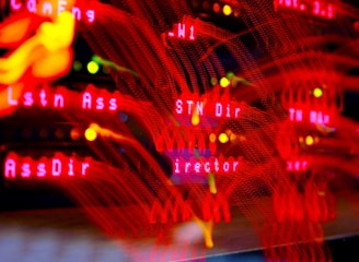 A close-up view of a server room or data center with bright red LED lights. The lights form various technical terms, suggesting network or server activity. The background is dark, highlighting the vibrant, dynamic lines and letters.