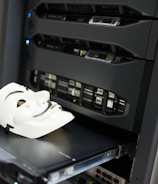 A white mask with distinct black features is placed on an open server tray in a data center or server room. The server is equipped with various LED indicators and network ports, suggesting an active setup.